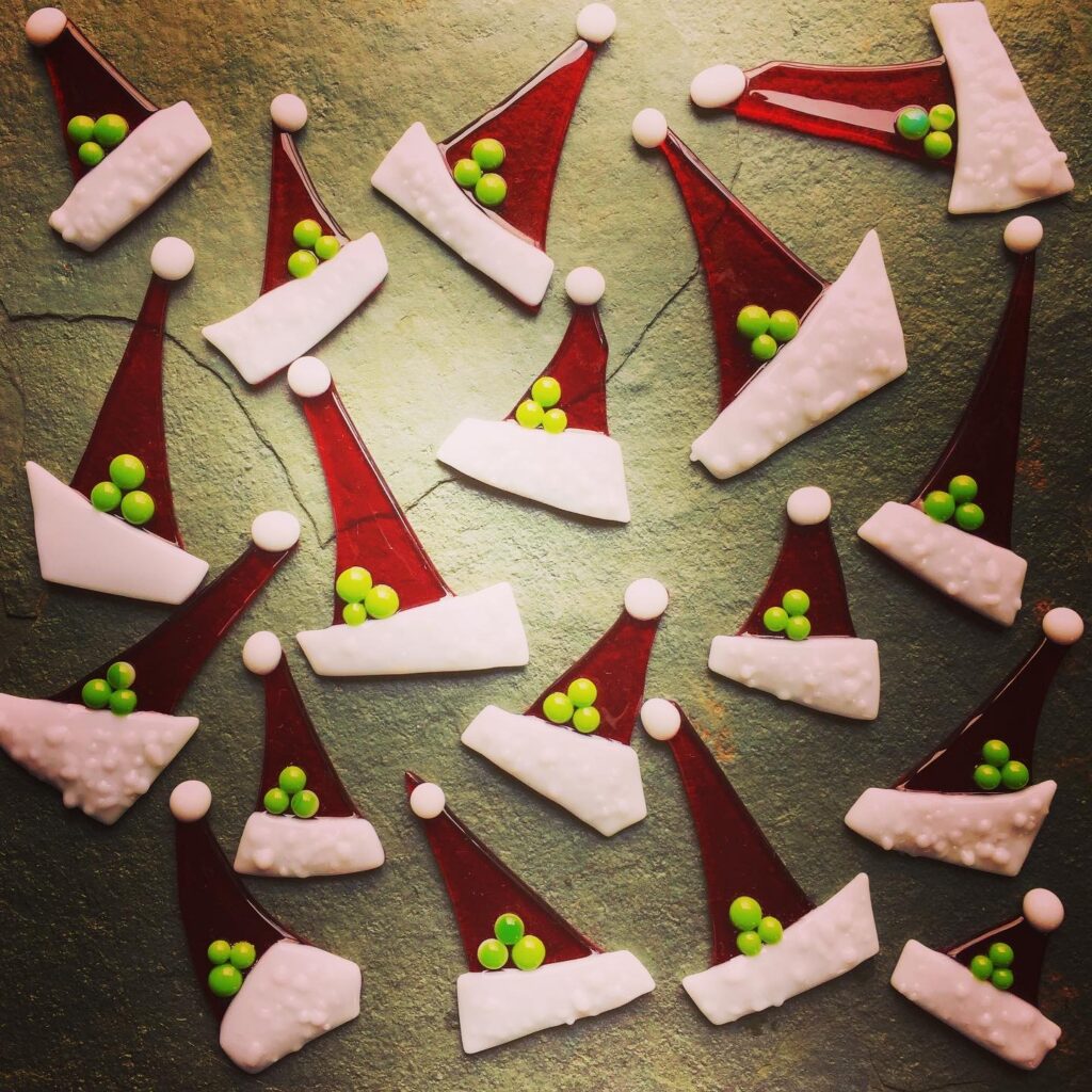 Santa's elf hats in red fused glass with white fur trim and green berries, made at the Fused Glass Christmas Decorations day class at Rainbow Glass Studios