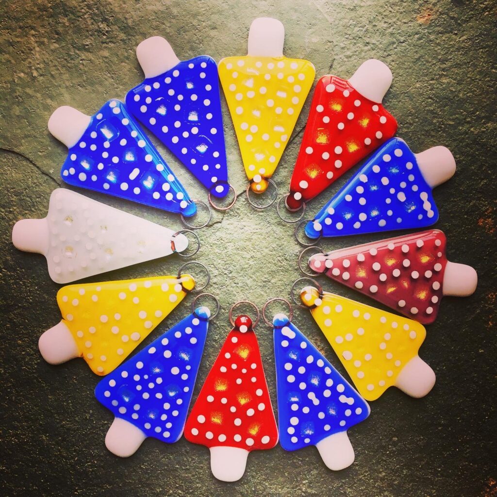 A carousel of Fused Glass Christmas trees in primary colours with snowy spots - to a design by Eleanor Watson at Rainbow Glass Studios