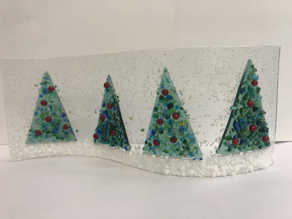 Fused Glass Snow scene with four green and red trees on a snowy landscape made at Rainbow Glass Studios