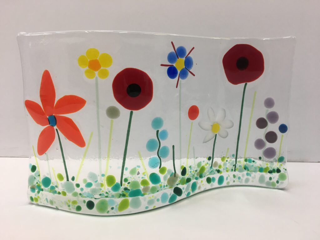 Fused glass field of flowers made on a glass wave that stands on it's edge - a lovely use of glass media and Frits in this creation by a beginner at Rainbow Glass Studios