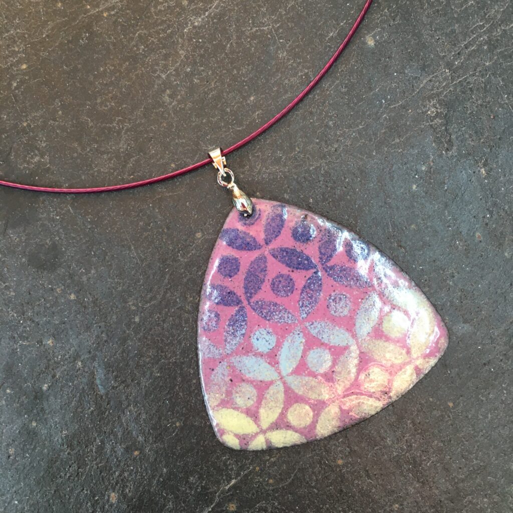 An enamelled pink, purple and white triangular pendant ready to wear home, made at Rainbow Glass Studios on the beginners day course