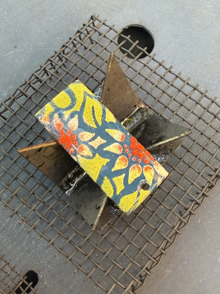 one enamelled pendant awaiting its next firing, a stencil has been used to make the pattern of flowers and leaves
