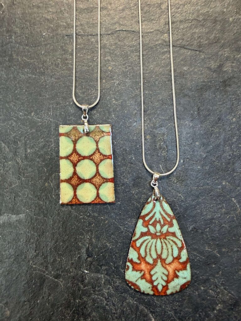 Two enamelled copper pendants on silver chains, showing the subtle colours and effects possible when enamelling jewellery at Rainbow Glass Studios