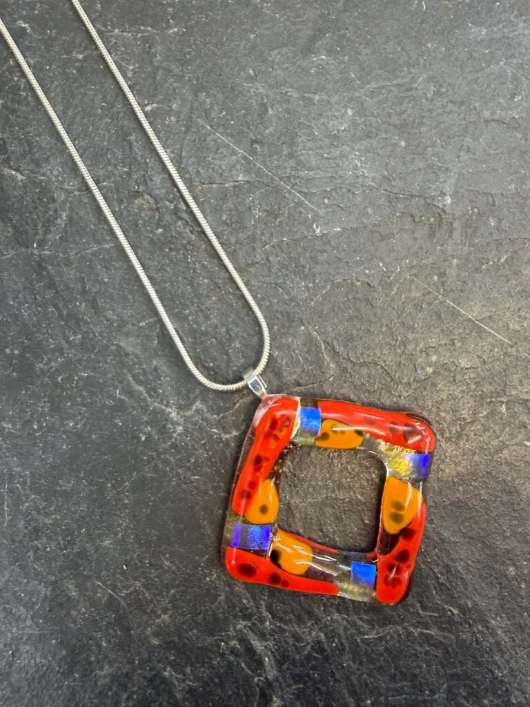 An intriguing square fused glass donut pendant in oranges, and blues, on a silver chain - made at Rainbow Glass Studios