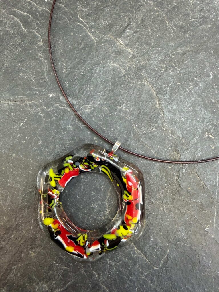 A fused glass donut pendant on a wire choker with an abstract design in black, yellow, red and white glass, a one of a kind unique creation on our jewellery day course in fused glass