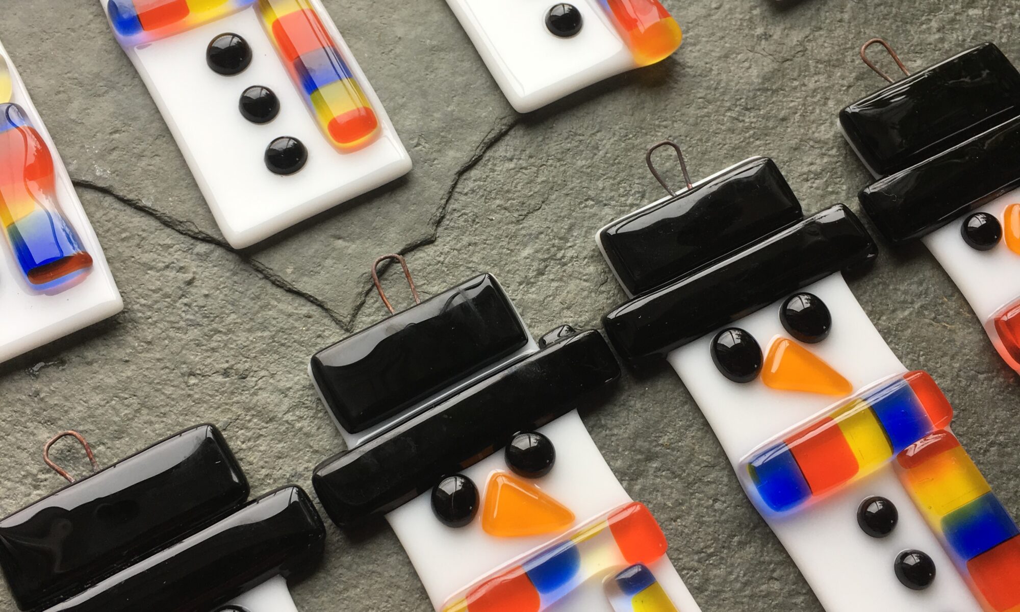A parade of Fused Glass Snowmen Christmas Decorations a design by Eleanor Watson of Rainbow Glass Studios